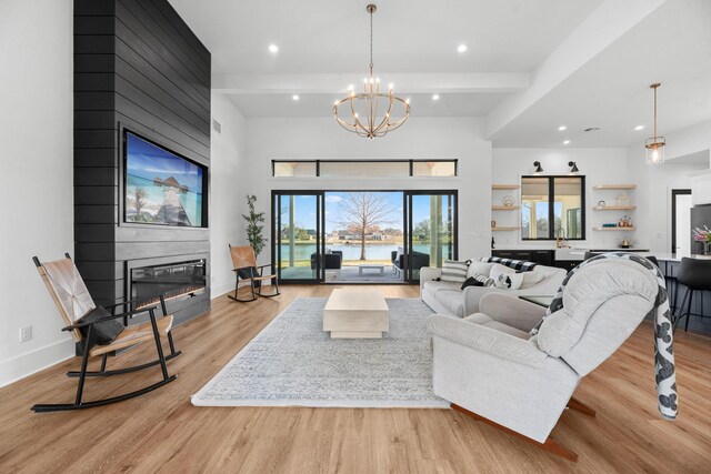 living room featuring beam ceiling, a fireplace, a chandelier, and light hardwood / wood-style flooring