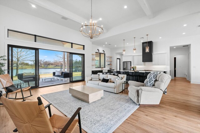 living room with a high ceiling, beamed ceiling, a chandelier, a water view, and light hardwood / wood-style flooring