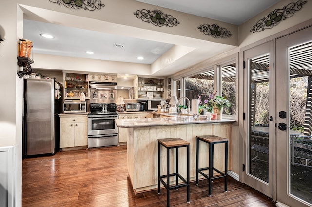 kitchen featuring dark wood-type flooring, a kitchen bar, sink, kitchen peninsula, and stainless steel appliances