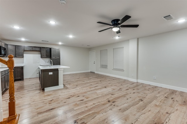 kitchen with an island with sink, light wood-type flooring, ceiling fan, sink, and tasteful backsplash