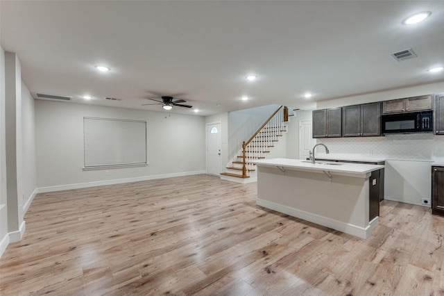 kitchen with a kitchen island with sink, a kitchen bar, sink, light hardwood / wood-style flooring, and backsplash