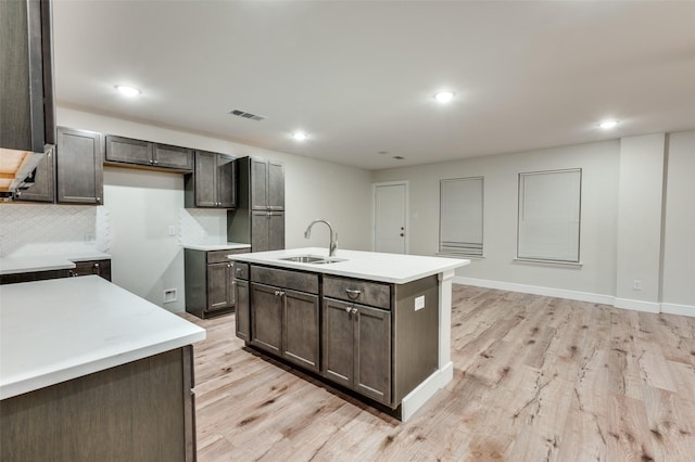 kitchen featuring a center island with sink, tasteful backsplash, light wood-type flooring, dark brown cabinets, and sink