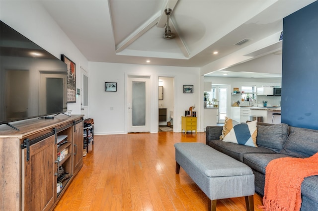 living room with ceiling fan, a tray ceiling, and light hardwood / wood-style flooring