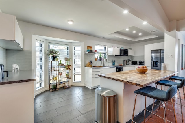 kitchen featuring white cabinets, stainless steel fridge, a breakfast bar area, and a wealth of natural light