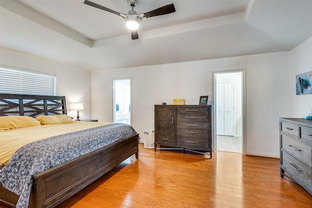 bedroom featuring connected bathroom, a tray ceiling, ceiling fan, and light hardwood / wood-style floors