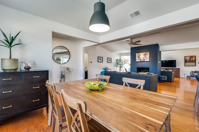 dining area featuring lofted ceiling with beams, ceiling fan, a fireplace, and light hardwood / wood-style flooring