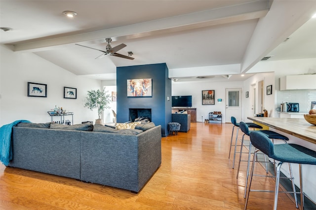 living room with vaulted ceiling with beams, ceiling fan, a fireplace, and light wood-type flooring