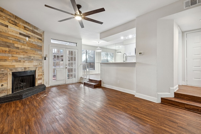 unfurnished living room featuring visible vents, a large fireplace, baseboards, wood finished floors, and a ceiling fan