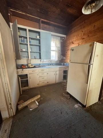 kitchen featuring white fridge, white cabinetry, wood walls, wooden ceiling, and sink