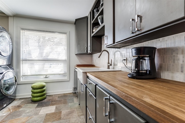 kitchen with wooden counters, tasteful backsplash, ornamental molding, sink, and stacked washer and dryer