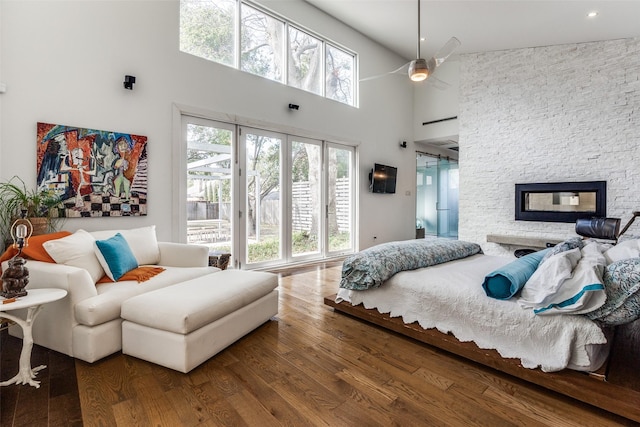 bedroom featuring access to exterior, ceiling fan, wood-type flooring, high vaulted ceiling, and a fireplace