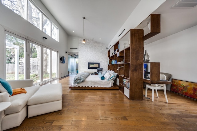 bedroom with hardwood / wood-style flooring, a stone fireplace, high vaulted ceiling, and multiple windows