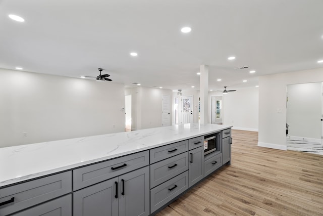 kitchen with ceiling fan, light stone countertops, gray cabinetry, and light hardwood / wood-style floors