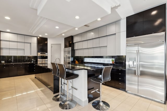 kitchen with stainless steel appliances, a kitchen breakfast bar, tasteful backsplash, an island with sink, and light tile patterned flooring