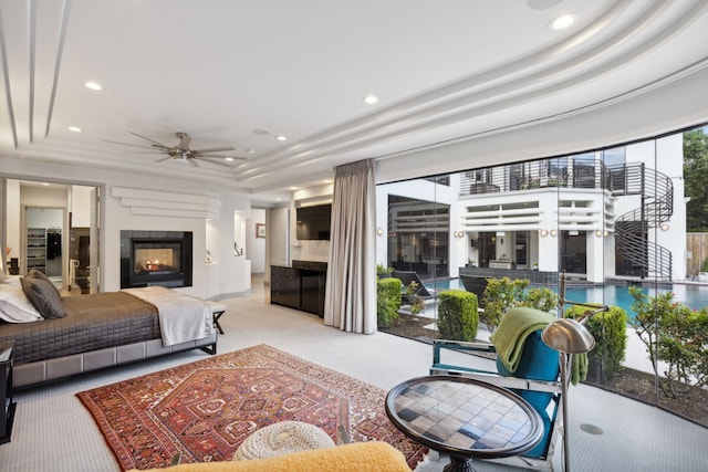 carpeted bedroom featuring a tray ceiling, ceiling fan, and a multi sided fireplace