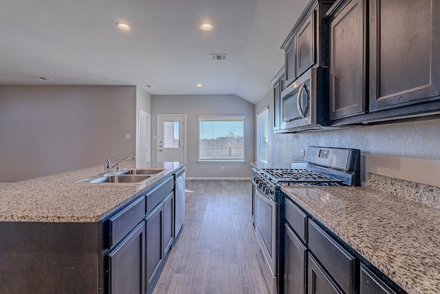 kitchen with dark brown cabinetry, stainless steel appliances, a kitchen island with sink, sink, and light hardwood / wood-style floors