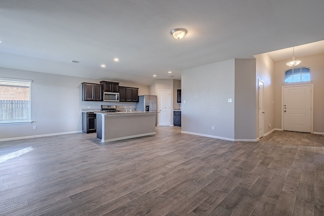 kitchen with hardwood / wood-style floors, plenty of natural light, stainless steel appliances, and a kitchen island with sink