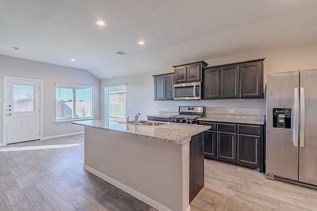 kitchen featuring light stone countertops, stainless steel appliances, vaulted ceiling, sink, and a center island with sink