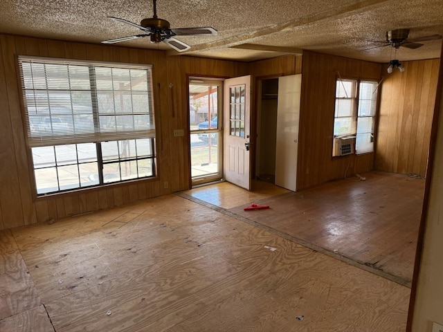 doorway to outside with a wealth of natural light, a textured ceiling, ceiling fan, and wood walls