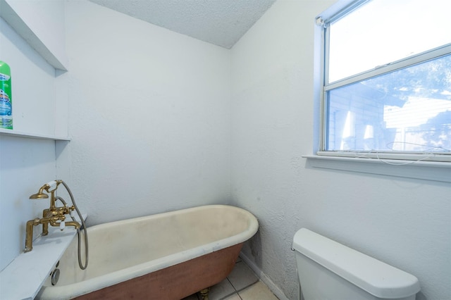 bathroom featuring a textured ceiling, a tub to relax in, toilet, and tile patterned flooring