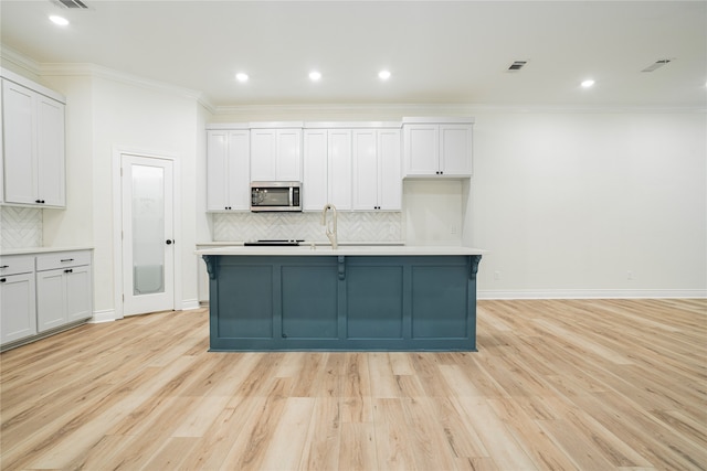 kitchen with an island with sink, crown molding, white cabinets, light hardwood / wood-style flooring, and tasteful backsplash