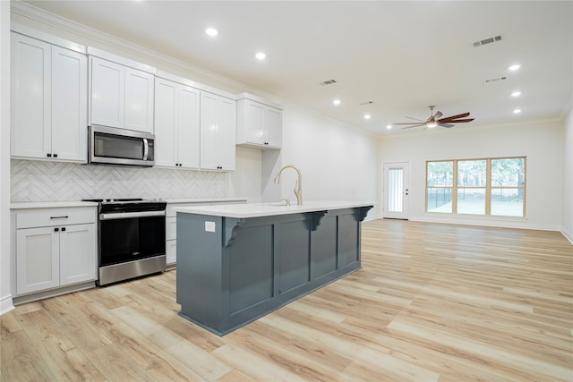 kitchen with stainless steel appliances, a center island with sink, backsplash, and white cabinetry