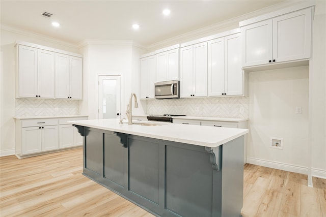 kitchen featuring sink, white cabinetry, crown molding, and a center island with sink