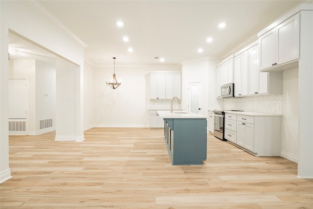 kitchen with appliances with stainless steel finishes, an island with sink, white cabinets, and decorative light fixtures