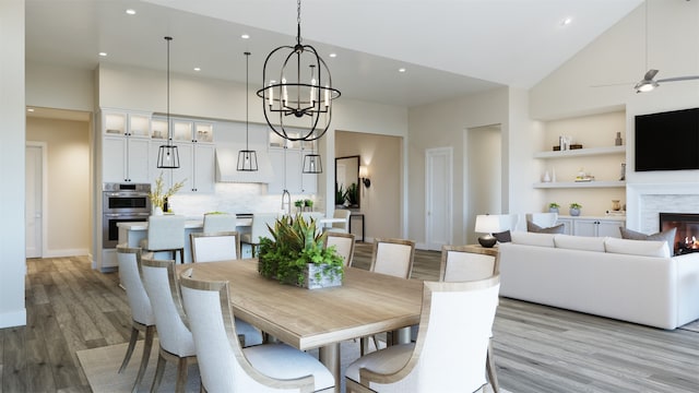 dining room with light wood-type flooring, built in shelves, ceiling fan with notable chandelier, sink, and high vaulted ceiling