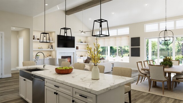 kitchen featuring a center island with sink, sink, beamed ceiling, light stone counters, and white cabinetry