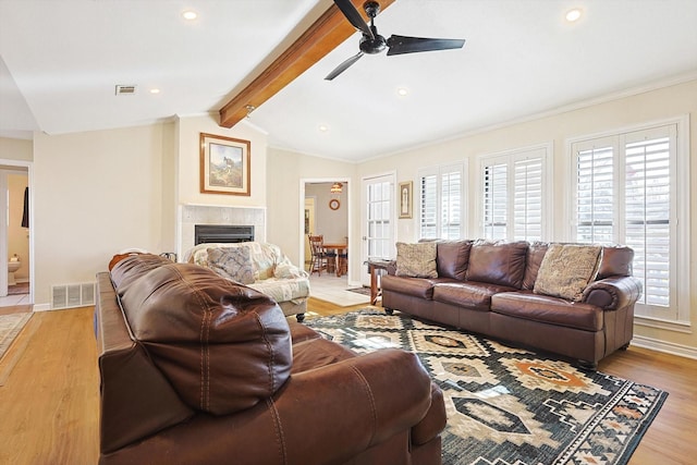 living room featuring vaulted ceiling with beams, a tile fireplace, light wood-type flooring, and ceiling fan