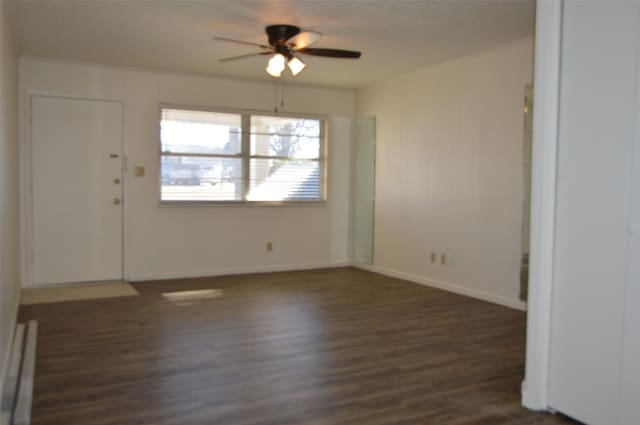 spare room featuring ceiling fan, dark wood-type flooring, and a baseboard heating unit