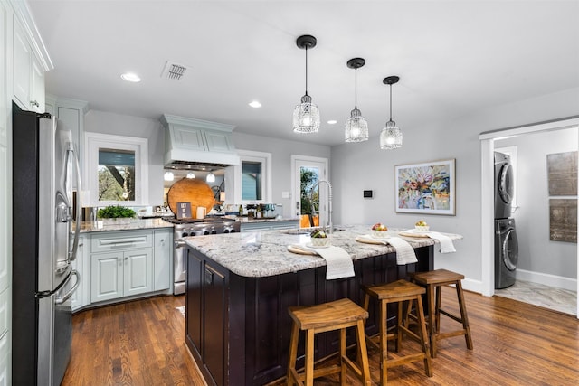 kitchen featuring stainless steel appliances, dark hardwood / wood-style flooring, light stone counters, and premium range hood