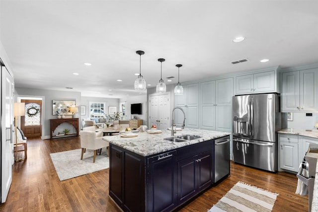 kitchen with stacked washer and dryer, stainless steel appliances, an island with sink, white cabinets, and sink