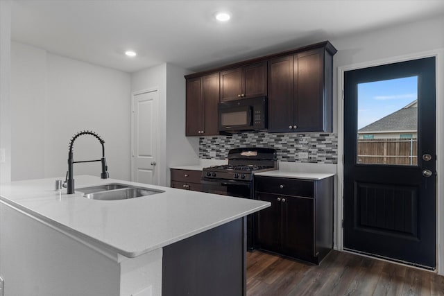 kitchen with tasteful backsplash, black appliances, sink, an island with sink, and dark hardwood / wood-style flooring