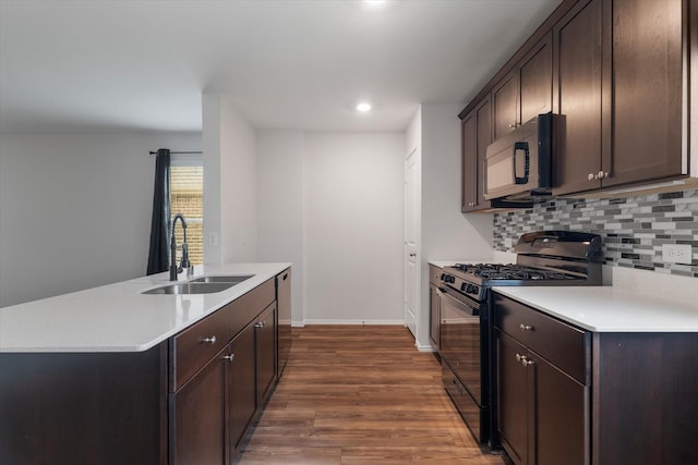 kitchen with sink, dark brown cabinets, a center island with sink, and black appliances