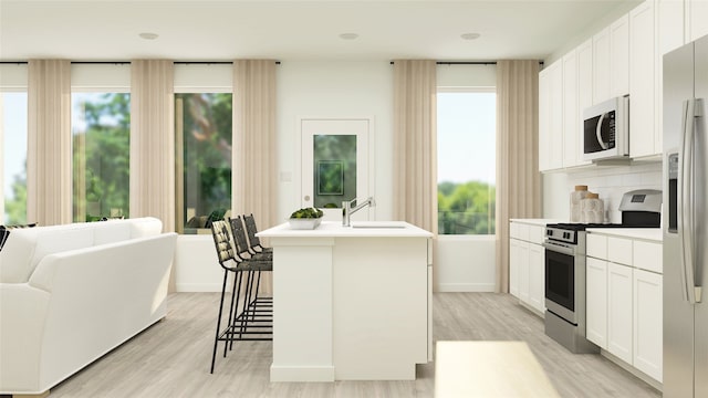 kitchen with backsplash, white cabinetry, stainless steel appliances, and an island with sink