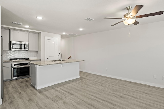 kitchen with gray cabinetry, a kitchen island with sink, sink, light stone countertops, and appliances with stainless steel finishes