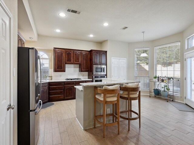 kitchen with a kitchen breakfast bar, decorative backsplash, light wood-type flooring, appliances with stainless steel finishes, and a kitchen island