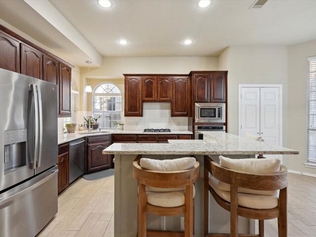 kitchen featuring light stone countertops, a center island, hanging light fixtures, a breakfast bar area, and appliances with stainless steel finishes