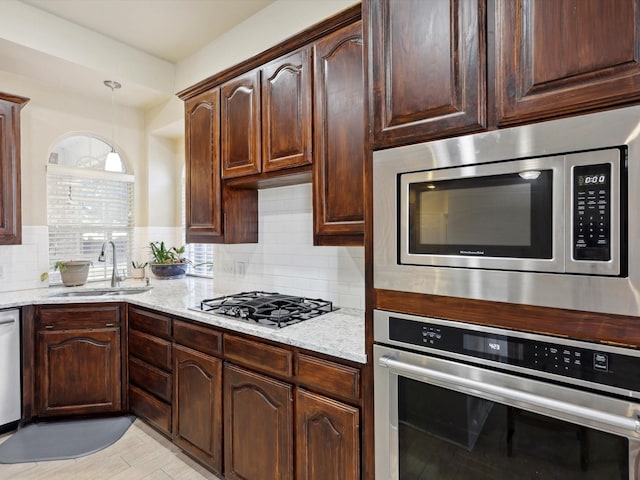 kitchen with light stone countertops, appliances with stainless steel finishes, backsplash, sink, and pendant lighting