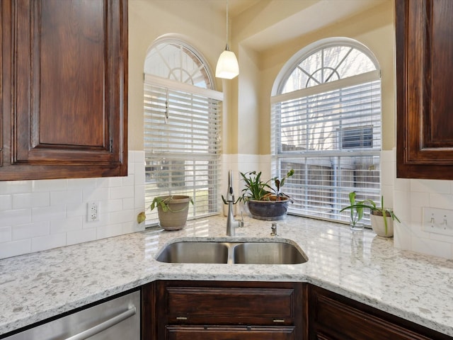 kitchen with pendant lighting, dishwasher, backsplash, sink, and light stone countertops