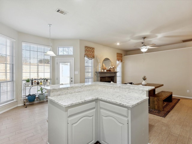 kitchen with ceiling fan, light stone countertops, decorative light fixtures, a kitchen island, and white cabinetry