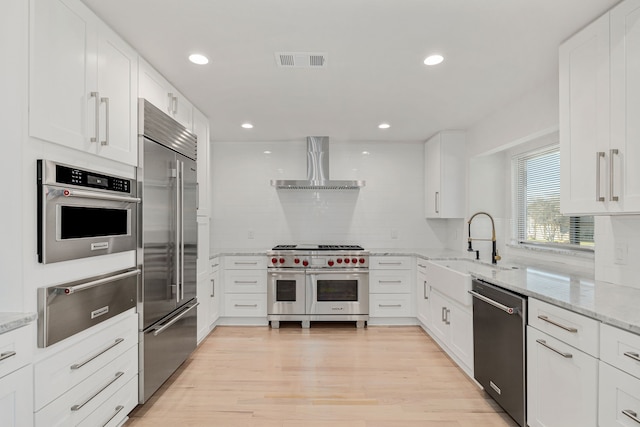 kitchen with white cabinets, wall chimney range hood, decorative backsplash, light stone countertops, and premium appliances