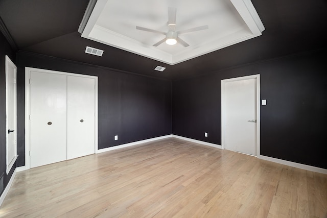 unfurnished bedroom featuring ceiling fan, a raised ceiling, light wood-type flooring, and a closet