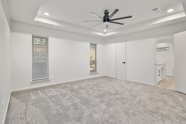 carpeted empty room with a raised ceiling and ceiling fan