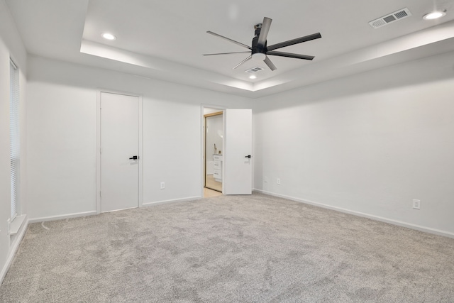 unfurnished bedroom with a tray ceiling, connected bathroom, ceiling fan, and light colored carpet