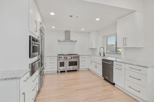 kitchen featuring sink, wall chimney exhaust hood, tasteful backsplash, white cabinetry, and stainless steel appliances