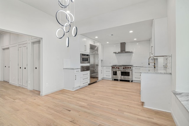 kitchen with light wood-type flooring, backsplash, wall chimney exhaust hood, high end appliances, and white cabinets