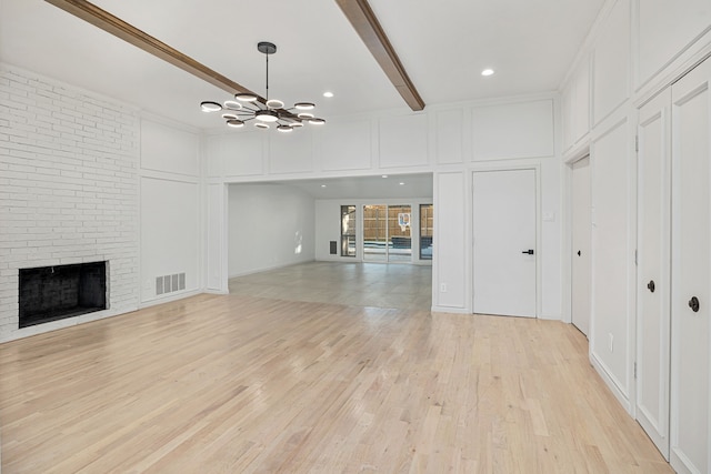 unfurnished living room featuring a chandelier, beam ceiling, light hardwood / wood-style floors, and a brick fireplace